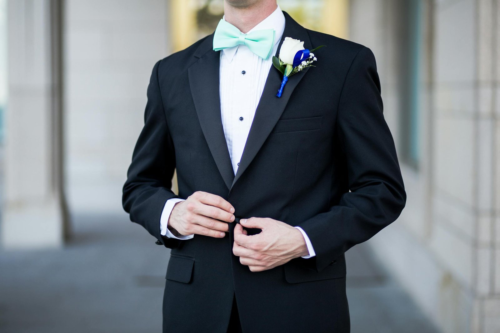 Sophisticated groom in a black tuxedo buttoning his jacket, adorned with a fresh boutonniere.